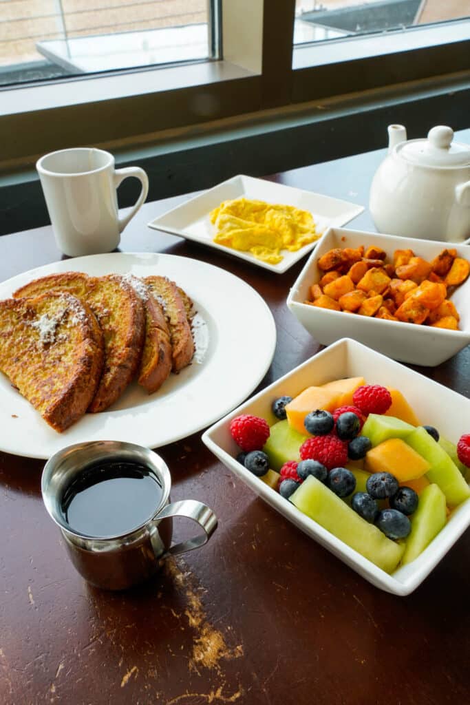 A breakfast spread of coffee, french toast, eggs, fresh fruit, and home fries. Located near the AC Hotel.